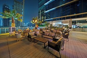 A rooftop bar with outdoor seating, palm trees, and a city skyline in the background.