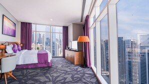 A hotel room with a large bed, a desk, a TV, and a view of the cityscape.