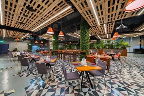 Un restaurant moderne avec un sol à motifs géométriques, des poutres en bois au plafond et des luminaires suspendus de couleur orange.