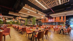 Un restaurante espacioso con mesas y sillas de madera, una zona de bar y un techo alto con vigas a la vista.