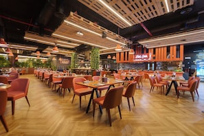 A spacious restaurant with wooden tables and chairs, a bar area, and a high ceiling with exposed beams.
