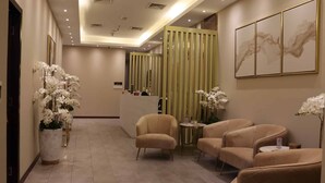 Vestíbulo de hotel con mostrador de recepción, zona de estar y detalles decorativos como orquídeas y obras de arte.