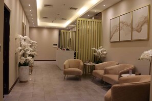 A hotel lobby with a reception desk, seating area, and decorative elements like orchids and artwork.