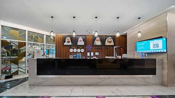 Un comptoir d’accueil d’hôtel au design moderne, doté d’un plan de travail en marbre, de panneaux en bois et de luminaires suspendus.