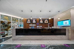 Un comptoir d’accueil d’hôtel au design moderne, doté d’un plan de travail en marbre, de panneaux en bois et de luminaires suspendus.