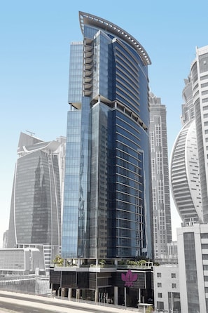 Un immeuble moderne de grande hauteur, doté d’une façade incurvée en verre, entouré d’autres bâtiments imposants.