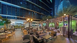 An outdoor lounge area with seating, a pergola, and a view of a modern building.