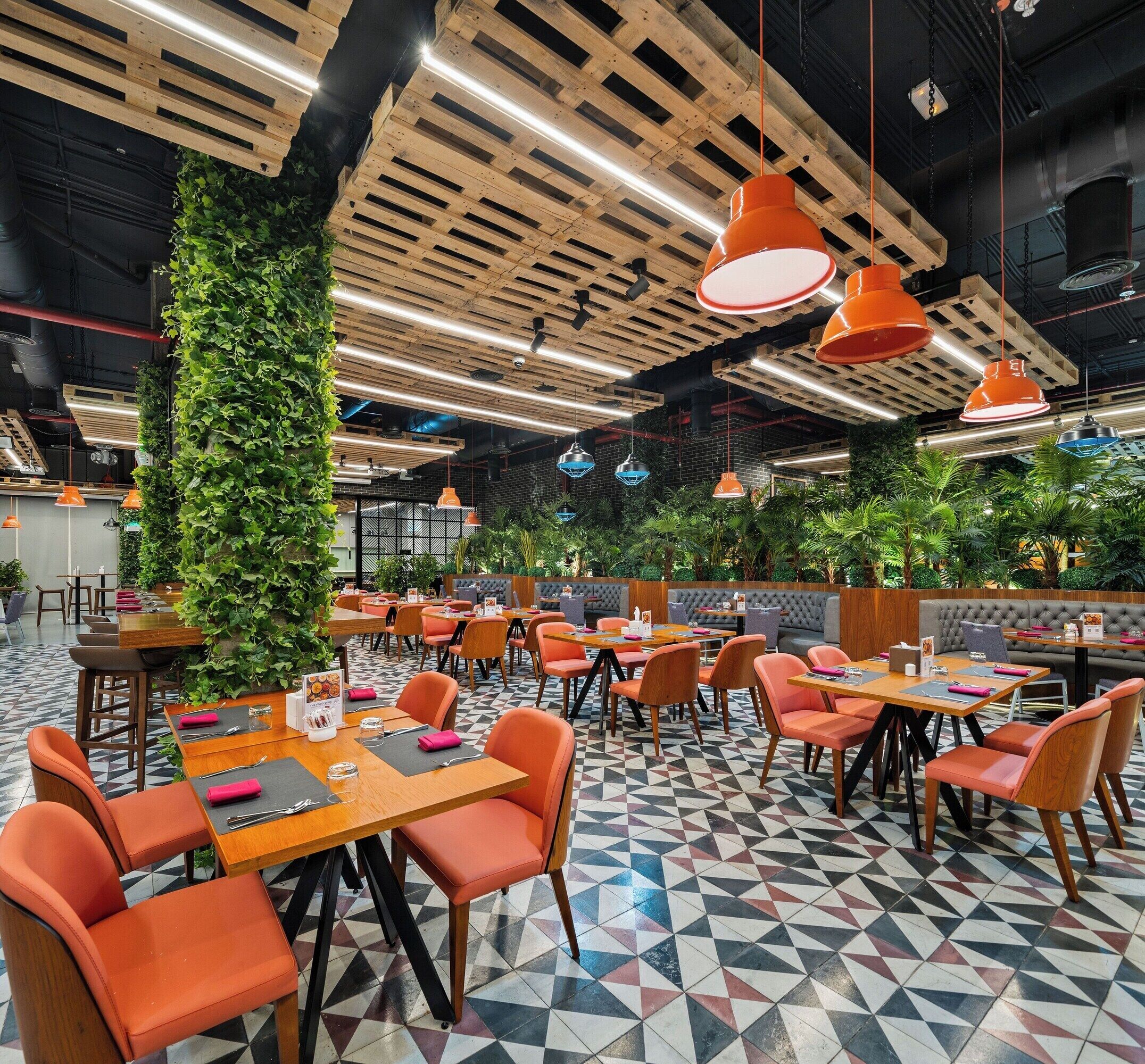 Un restaurant avec des poutres en bois au plafond, des luminaires suspendus de couleur orange et un sol orné de motifs géométriques.