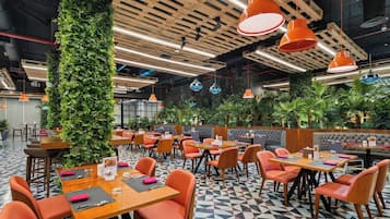 Un restaurant avec des poutres en bois au plafond, des luminaires suspendus de couleur orange et un sol orné de motifs géométriques.