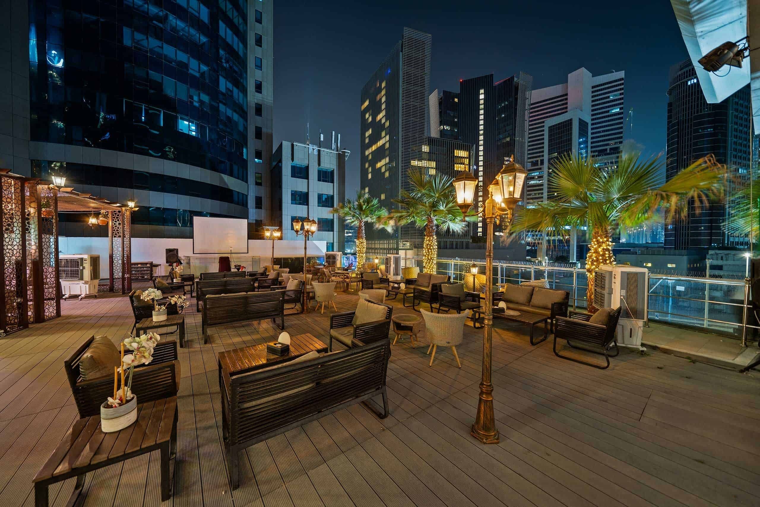 Un bar situé sur le toit d’un immeuble, avec une terrasse, des palmiers et une vue imprenable sur le paysage urbain.