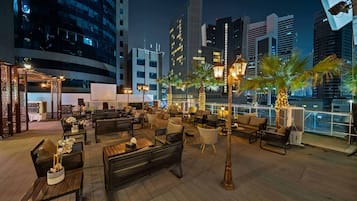 Un bar situé sur le toit d’un immeuble, avec une terrasse, des palmiers et une vue imprenable sur le paysage urbain.