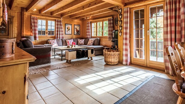 Ein Holzblockhaus-Interieur mit hohen Decken, einer Sofagarnitur, einem Esstisch und großen Fenstern.