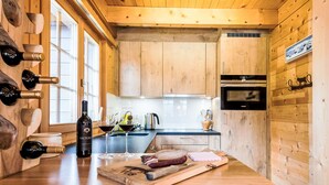 Ein Holzinterieur mit einer Küchenarbeitsplatte, Weinflaschen, Gläsern und einem Schneidebrett mit Fleisch.