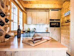 Ein Holzinterieur mit einer Küchenarbeitsplatte, Weinflaschen, Gläsern und einem Schneidebrett mit Fleisch.
