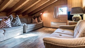 Ein gemütliches Dachzimmer mit Holzbalken, einer Couch, einem Sessel und einem Fernseher.
