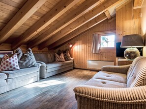 Ein gemütliches Dachzimmer mit Holzbalken, einer Couch, einem Sessel und einem Fernseher.