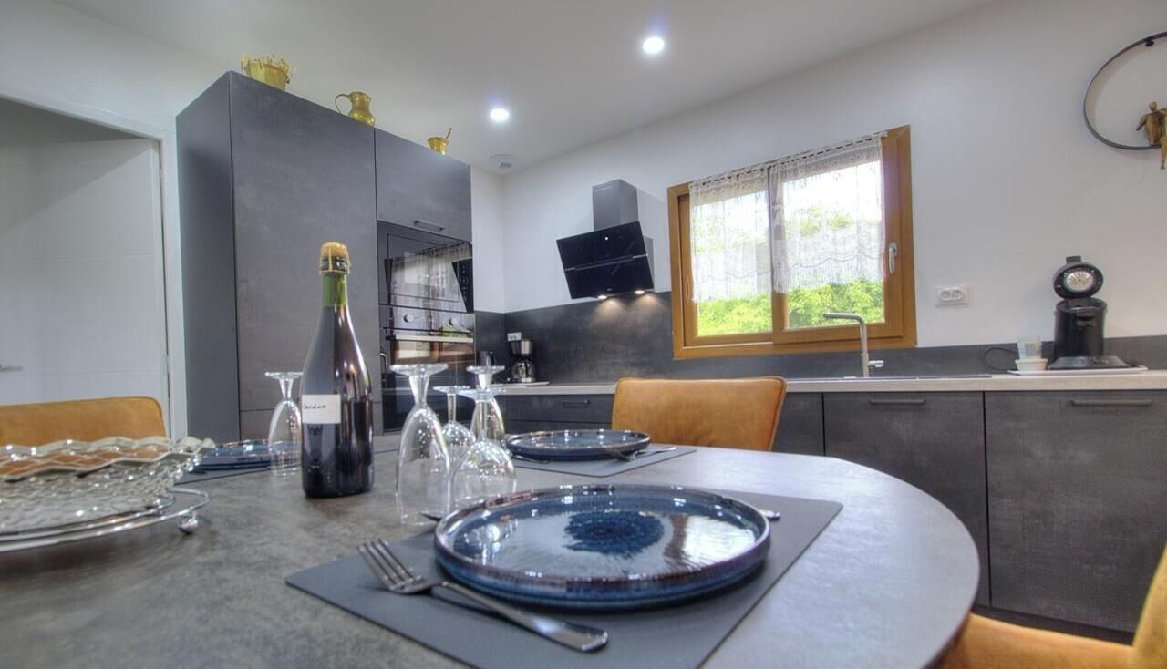 A modern kitchen with a dining table set for two, a bottle of champagne, and a coffee machine.