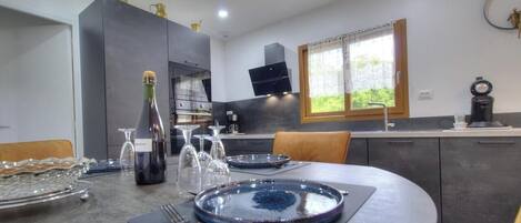A modern kitchen with a dining table set for two, a bottle of champagne, and a coffee machine.