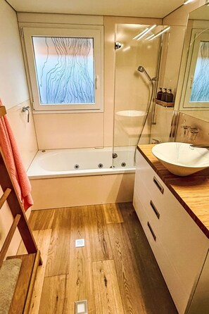 Un baño moderno con bañera, cabina de ducha de vidrio, suelo de madera y un espejo grande.