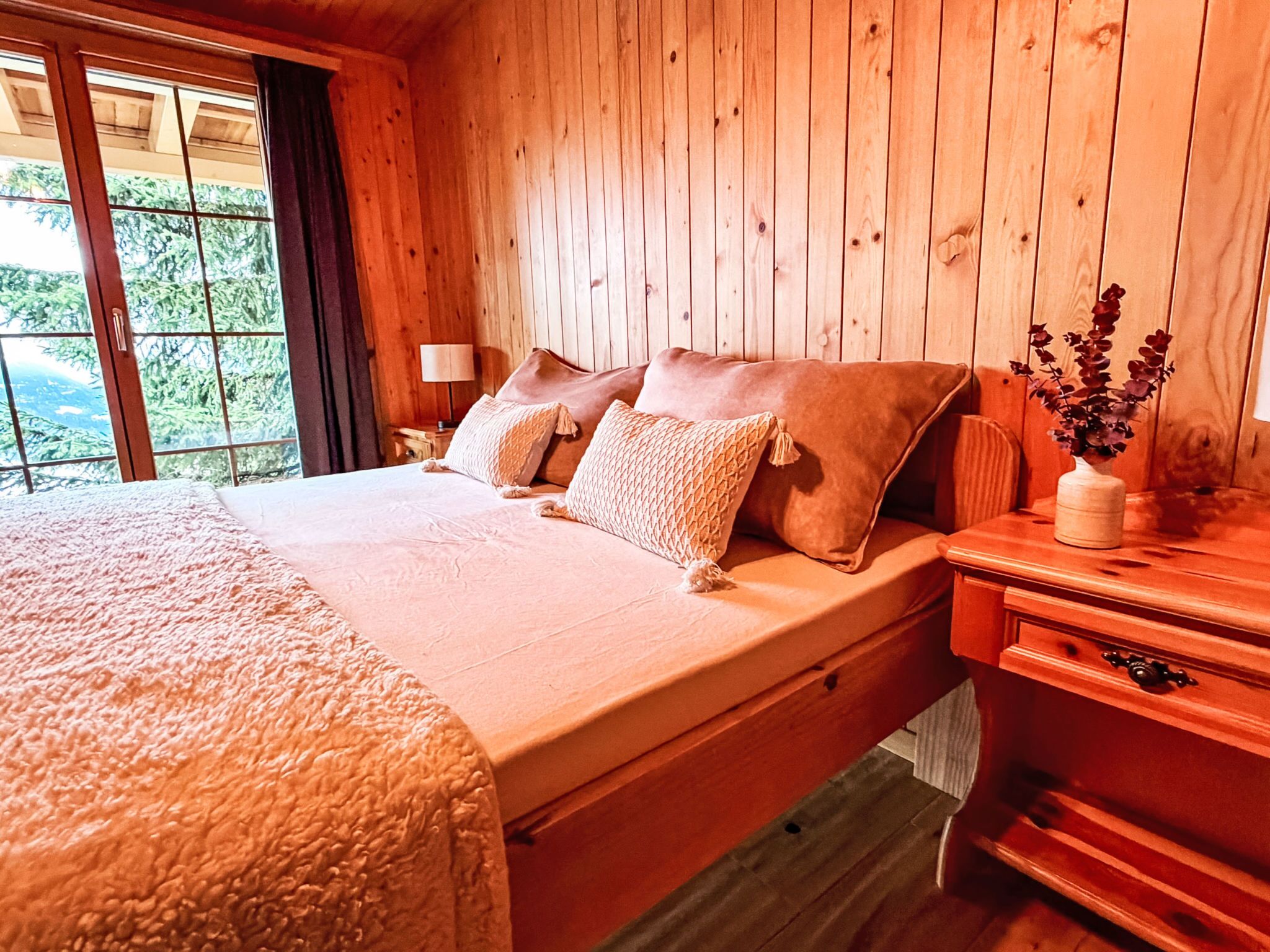 Ein Zimmer mit Holzboden, einem Bett, einem Nachttisch, einer Lampe und einer Vase mit Blumen.