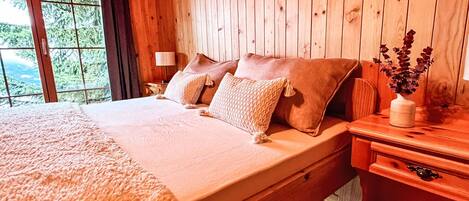 Ein Zimmer mit Holzboden, einem Bett, einem Nachttisch, einer Lampe und einer Vase mit Blumen.