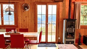 L’intérieur d’un chalet en bois comprend un coin repas, une cheminée et une vue dégagée grâce aux grandes fenêtres.