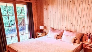 Une chambre à coucher en bois, avec un grand lit, une table de chevet, une lampe et une fenêtre avec des rideaux.