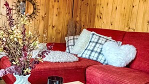 Un intérieur en bois avec un canapé rouge, un vase blanc contenant des fleurs séchées et trois bougies disposées sur un plateau en bois.