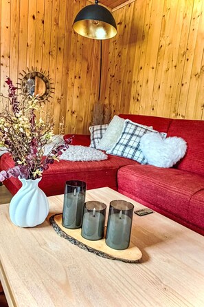 A wooden interior with a red sofa, a white vase with dried flowers, and three candles on a wooden tray. - La Marmotte by Interhome (Bellwald)