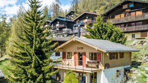 Un bâtiment de style chalet, doté d’un balcon et entouré d’arbres ainsi que d’autres bâtiments de style chalet.