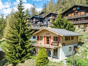 A chalet-style building with a balcony, surrounded by trees and other chalet buildings. - La Marmotte by Interhome (Bellwald)