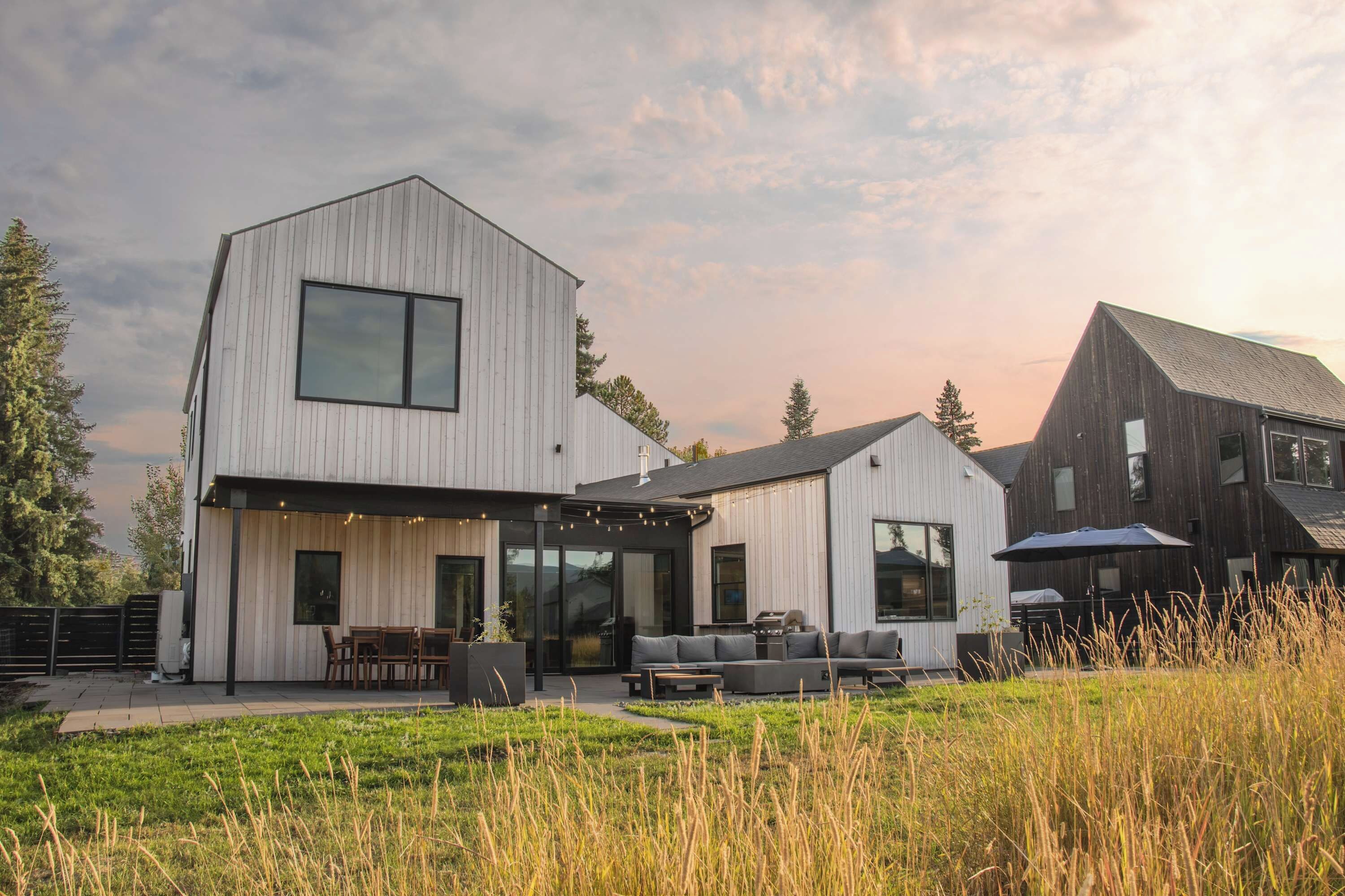 Une maison moderne à deux étages, dotée d’un toit plat, de grandes fenêtres et d’un espace extérieur aménagé avec un coin salon couvert.