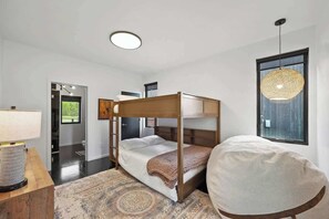 A bedroom with a bunk bed, a round hanging light fixture, a patterned rug, and a bedside table with a lamp. - Whitefish Modern Escape (Whitefish)