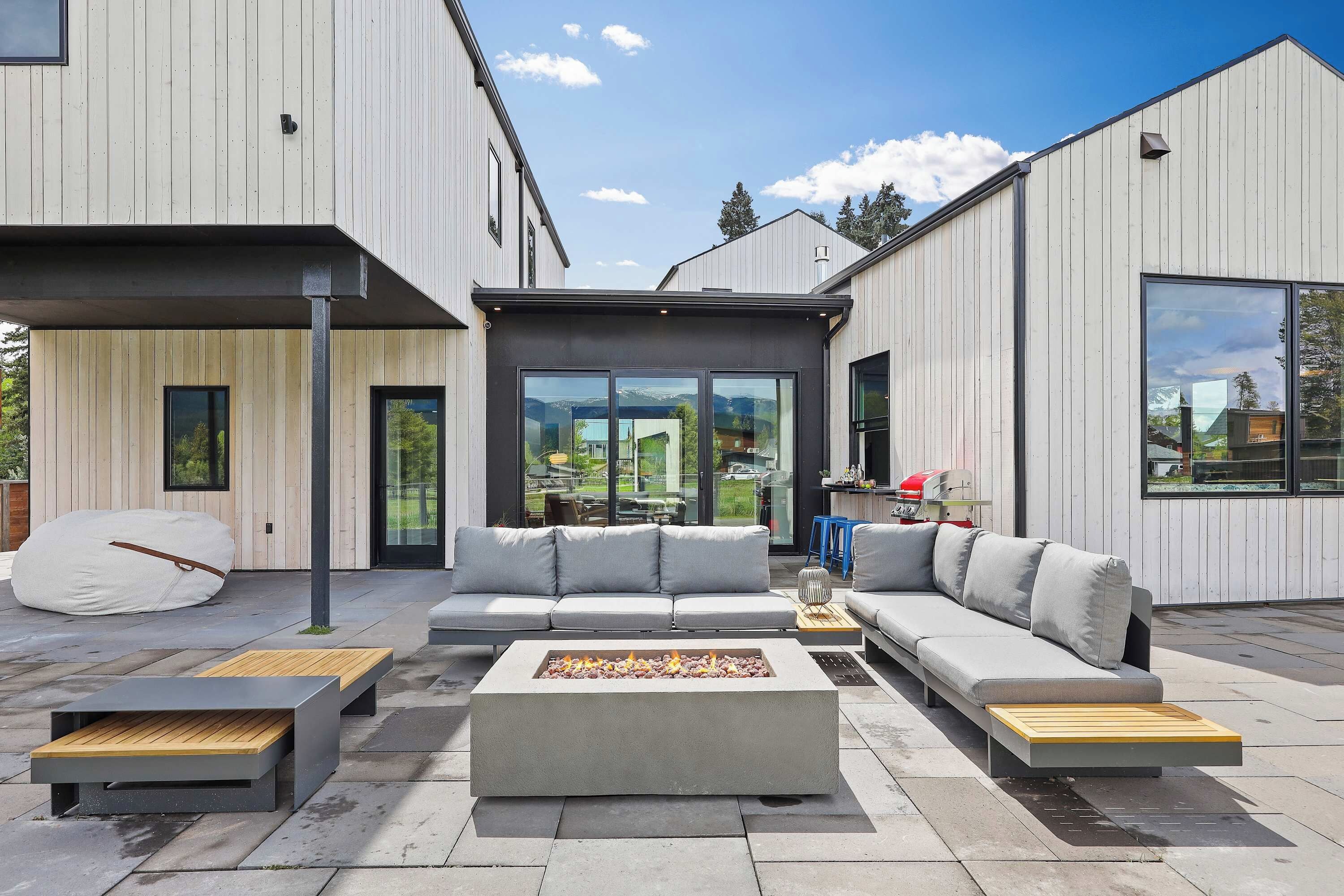 A modern outdoor living area with a sectional sofa, a fire pit, and a wooden bench.