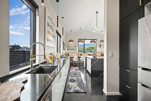 A modern kitchen with a large window, a black countertop, and a stainless steel refrigerator. - Whitefish Modern Escape (Whitefish)