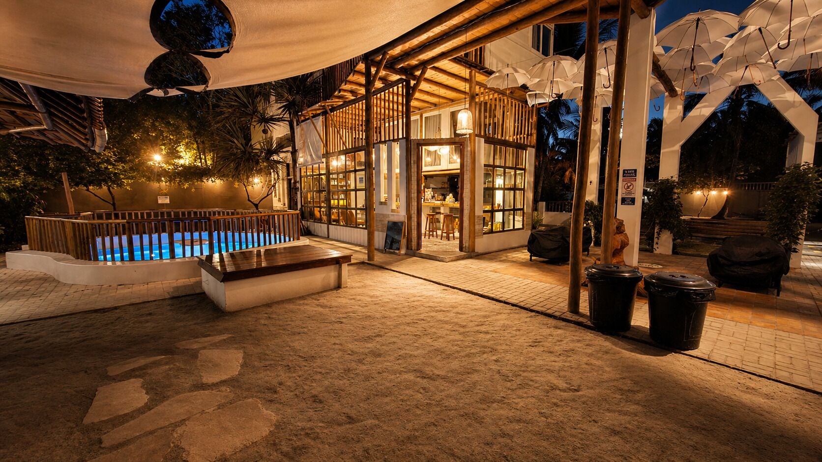 An outdoor pool area with a wooden deck, a seating area, and a covered section with umbrellas.