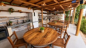 An outdoor dining area with wooden tables and chairs, surrounded by a rustic wooden pergola. - Glamping Med (Porto Seguro)
