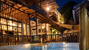 A swimming pool with a stone floor, surrounded by a wooden deck and a building with multiple balconies. - Glamping Med (Porto Seguro)