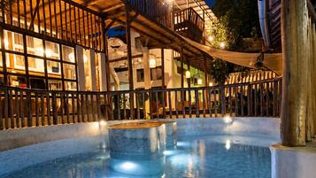 A swimming pool with a stone floor, surrounded by a wooden deck and a building with multiple balconies.