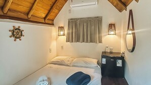 A bedroom with a sloped ceiling, a bed with pillows, a bedside table with a lamp, and a wall-mounted air conditioning unit. - Glamping Med (Porto Seguro)