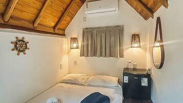 A bedroom with a sloped ceiling, a bed with pillows, a bedside table with a lamp, and a wall-mounted air conditioning unit.