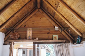 Teto de madeira com um vértice triangular, uma estante com uma placa e uma janela com cortinas.