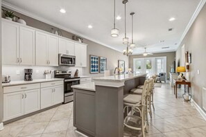 A modern kitchen with white cabinets, a central island, and pendant lighting. - Beautifully designed townhouse nestled in the wooded charm of Amelia Island (Fernandina Beach)