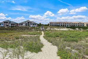 Ein Weg führt zu einem Strandhotel mit mehreren Balkonen und blauem Himmel.
