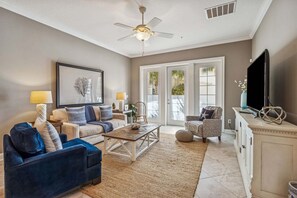 A living room with a ceiling fan, a coffee table, sofas, a TV, and a cabinet. - Beautifully designed townhouse nestled in the wooded charm of Amelia Island (Fernandina Beach)