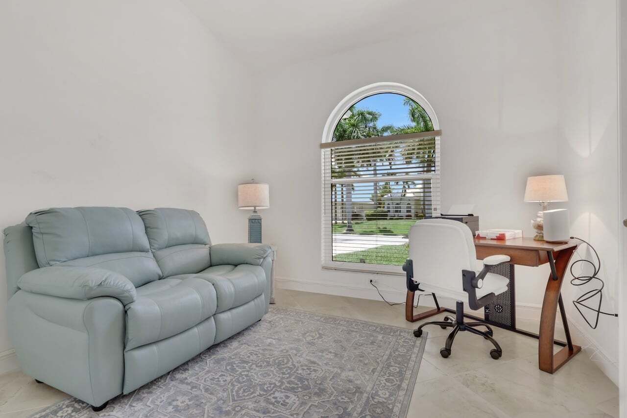 A room with a light blue sofa, a desk with a chair, a lamp, and a window with blinds.