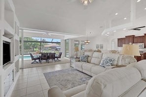 A spacious living room with a large sofa, a dining area with a table and chairs, and a kitchen area with wooden cabinets and a microwave. - Villa Sandcastle 1003 Southern Exposure SW Cape Heated Pool Home w/ Kayaks (Cape Coral)