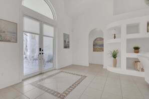 A spacious hallway with a large glass door leading to a snowy outdoor scene, white walls, and a tiled floor. - Villa Sandcastle 1003 Southern Exposure SW Cape Heated Pool Home w/ Kayaks (Cape Coral)