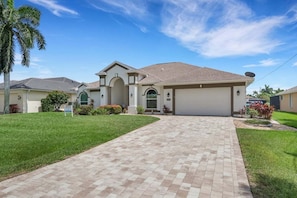 A residential house with a driveway, a garage, and a well-maintained lawn. - Villa Sandcastle 1003 Southern Exposure SW Cape Heated Pool Home w/ Kayaks (Cape Coral)