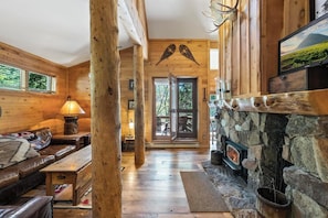 L’intérieur d’une cabane en rondins, avec une cheminée en pierre, des murs en bois, un canapé en cuir et un banc.